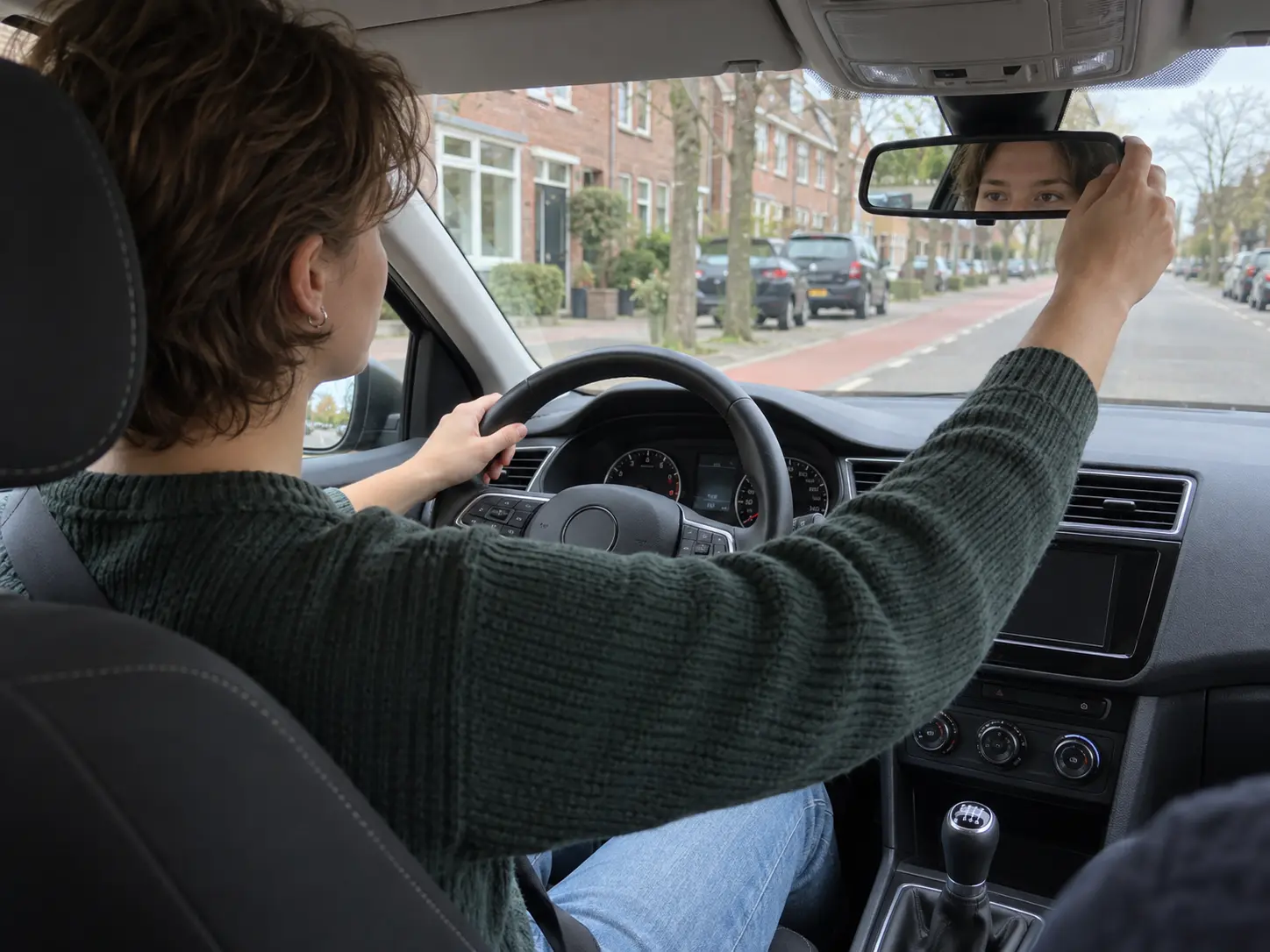 Leerling stelt de binnenspiegel af in een lesauto op een Nederlandse woonstraat