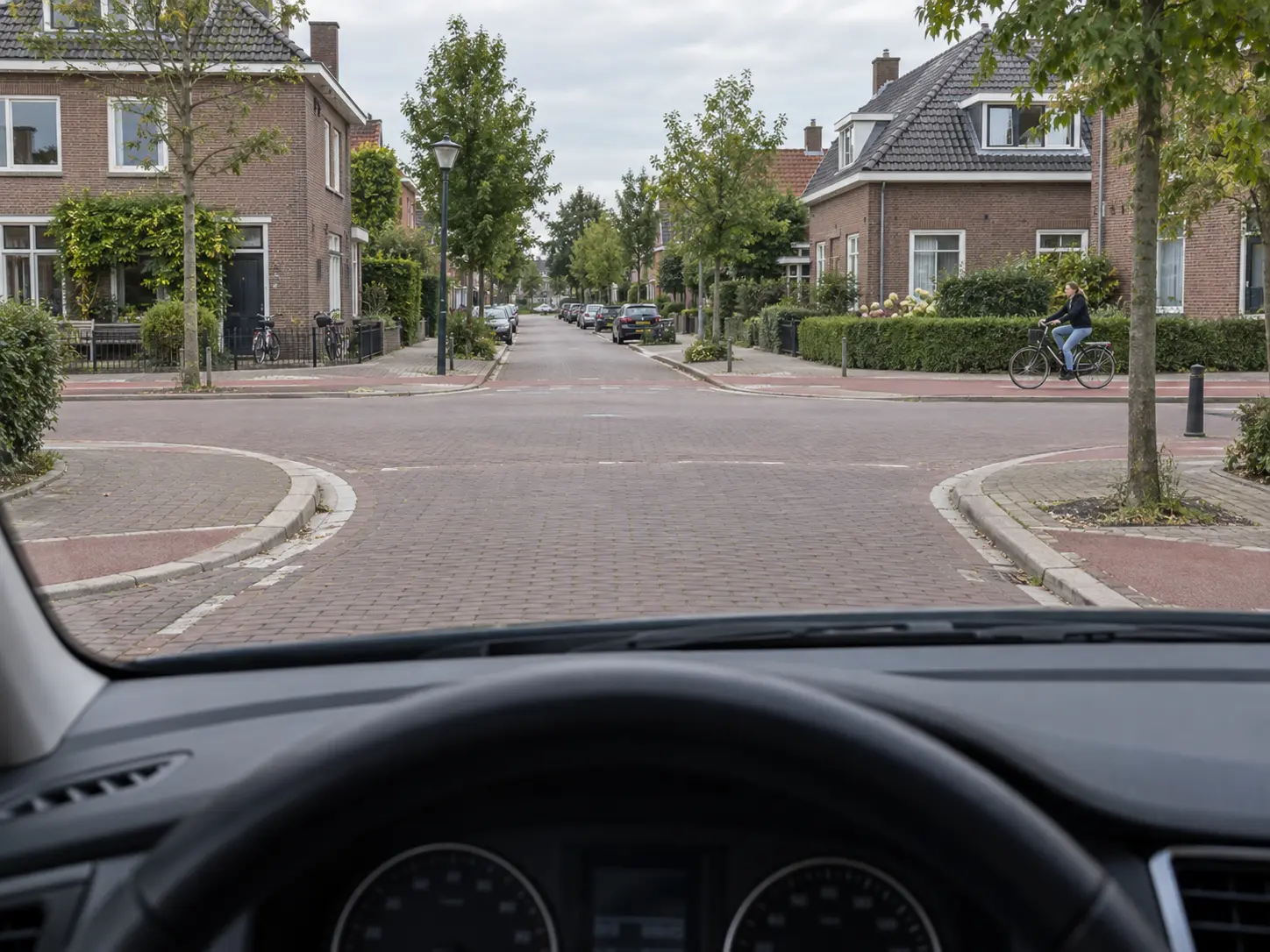 Zicht vanuit een lesauto op een kruispunt in een Nederlandse woonwijk met een fietser