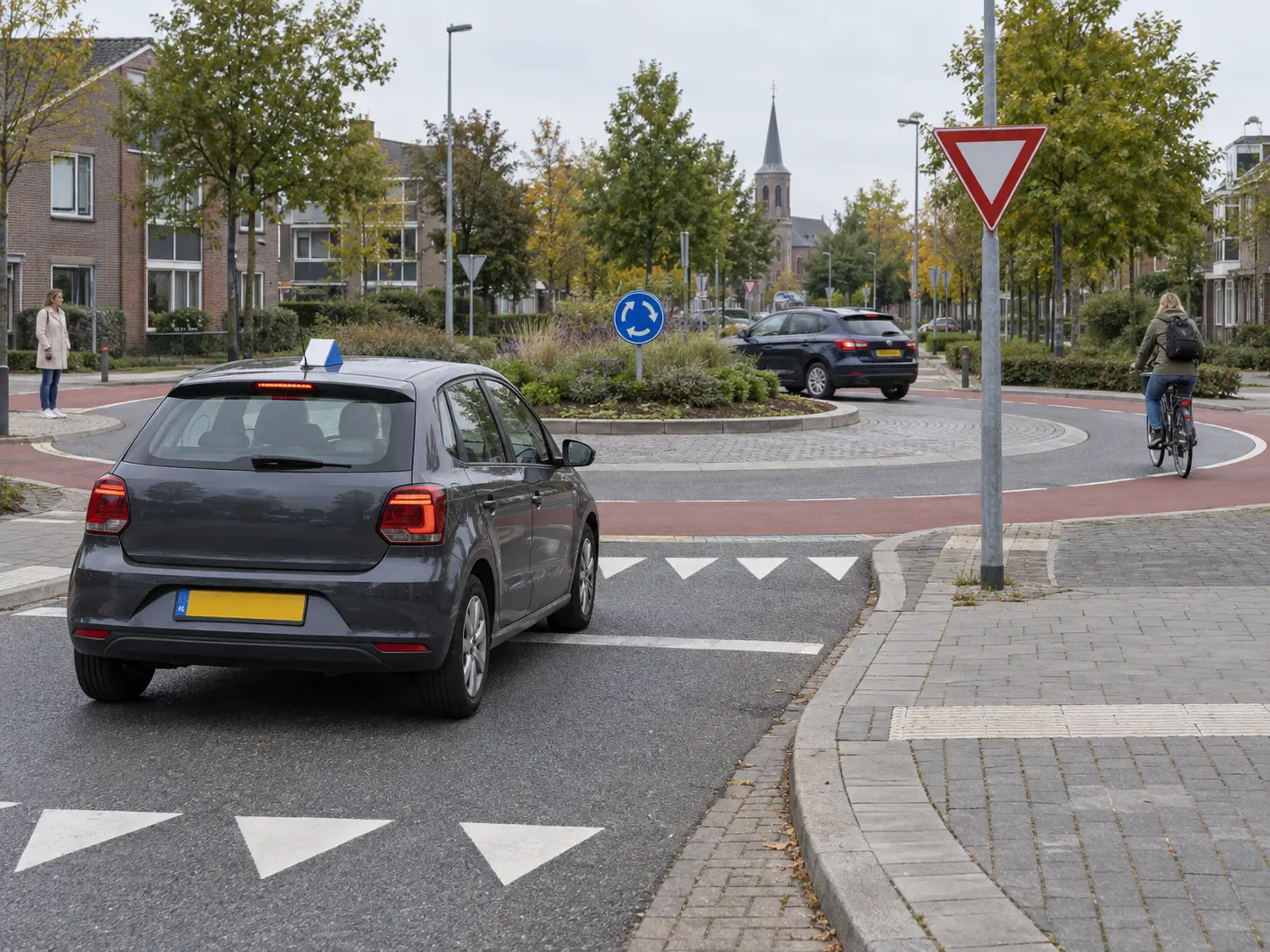 Lesauto wacht voor een Nederlandse rotonde met een fietser en ander verkeer