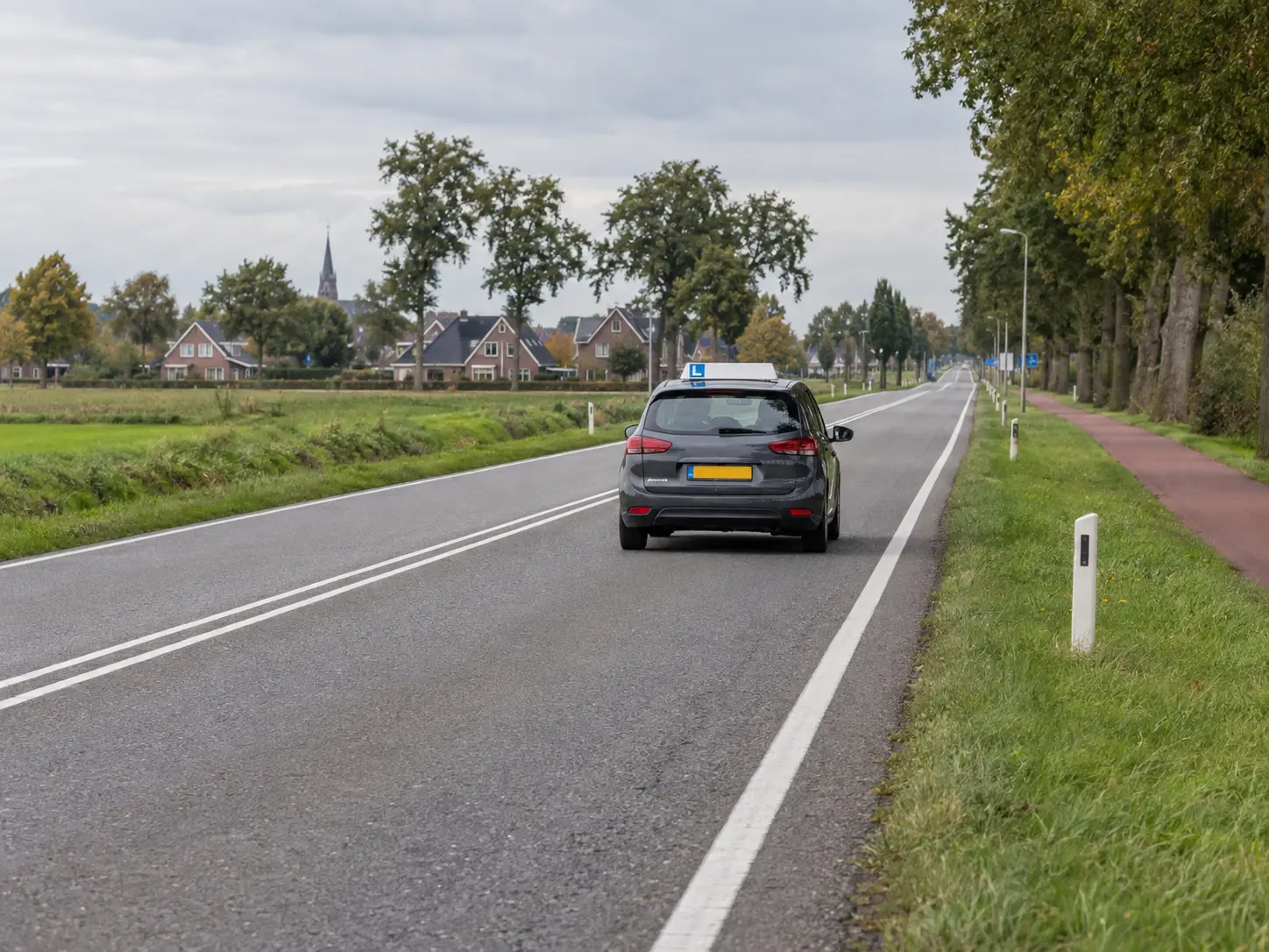 Lesauto rijdt op een Nederlandse provinciale weg langs een rood fietspad